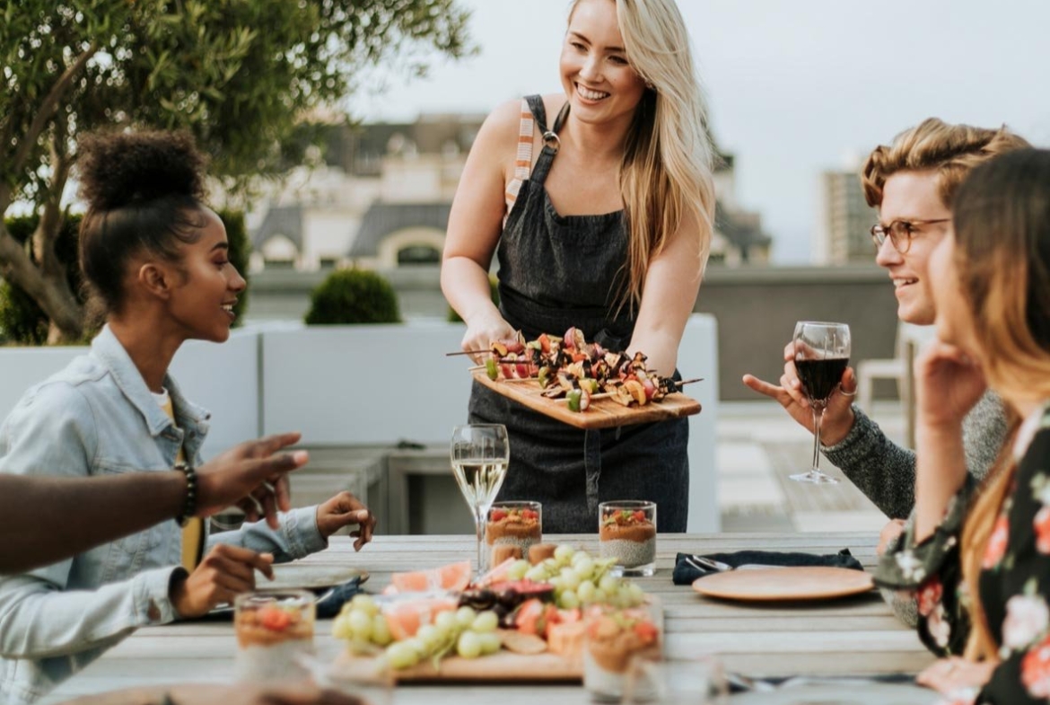 A woman serving food to a group of people at an outdoor table.