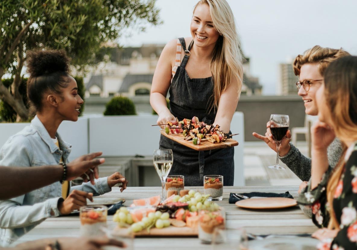 A woman serving food to a group of people at an outdoor table. A woman serving food to a group of people at an outdoor table.