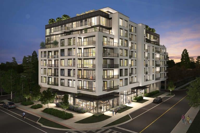 A modern multi-story apartment building, 35 Plains Road Condos, features numerous windows and balconies illuminated at dusk. The structure showcases a mix of white and glass exterior elements. Surrounding the building are sidewalks, streetlights, a few people walking, and landscaped greenery.