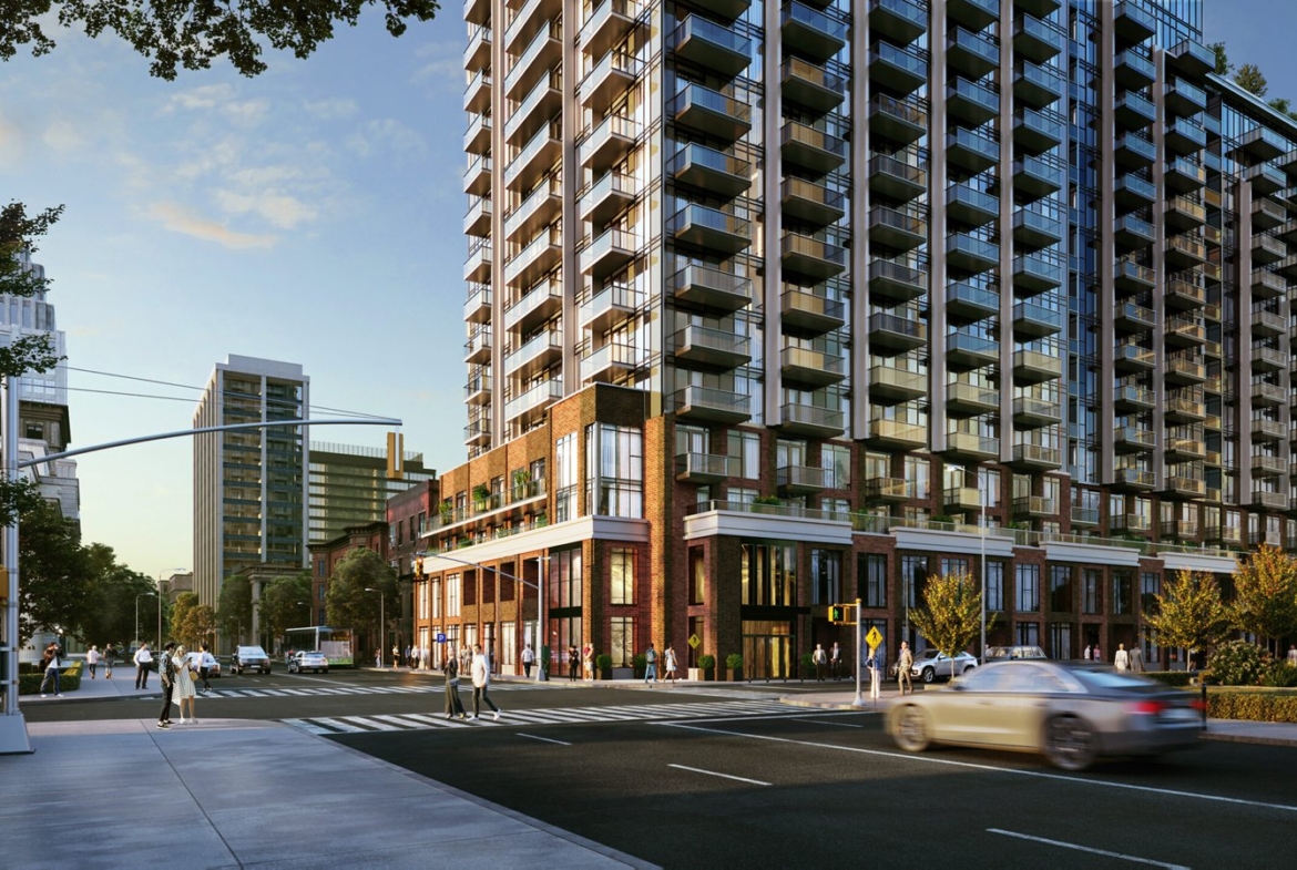 A modern, high-rise apartment building stands on a busy city street corner during the day. People are walking along the sidewalks, and cars are driving past. The building features many balconies and is surrounded by other tall structures and greenery, showcasing new condos in GTA.
