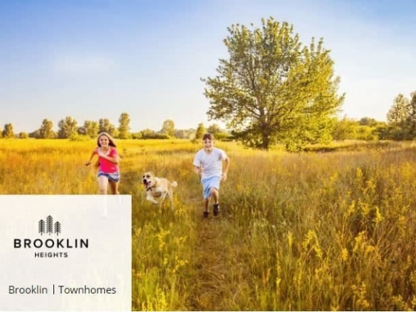 A young man and woman run joyfully with a golden retriever through a sunlit field of tall grass, with trees in the background under a clear blue sky. In the bottom left corner, a Brooklin Heights townhomes logo and text that reads "Brooklin Heights | Townhomes" are displayed.