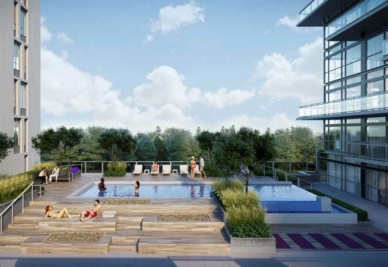 A modern rooftop pool area with two pools surrounded by lounge chairs, plants, and people relaxing. The area is bordered by tall glass buildings and overlooks a green, tree-filled landscape beneath a partly cloudy sky—an oasis that new condos in the GTA can offer.