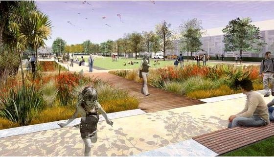 A park scene with people walking on paths and sitting on benches. Trees and shrubs are plentiful, and some people in the background are flying kites. The area is landscaped with plants lining the paths, adjacent to new homes under construction, and a grassy field is in the center.