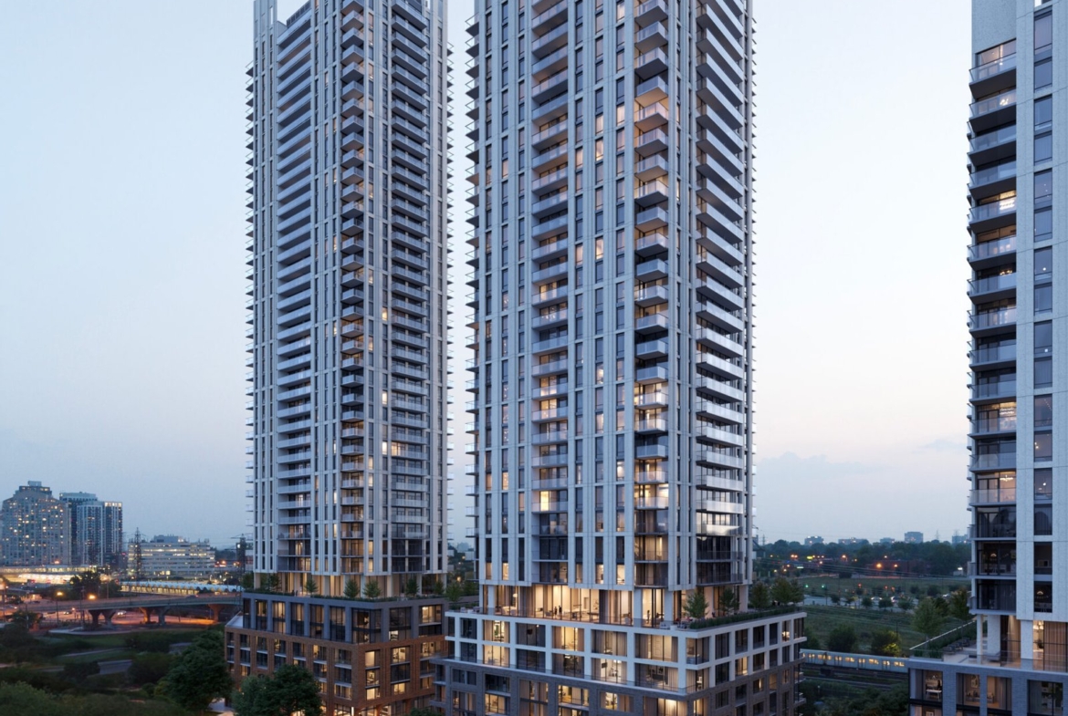 Aerial view of modern twin high-rise New condos at dusk, illuminated, with surrounding greenery and a road at the base.