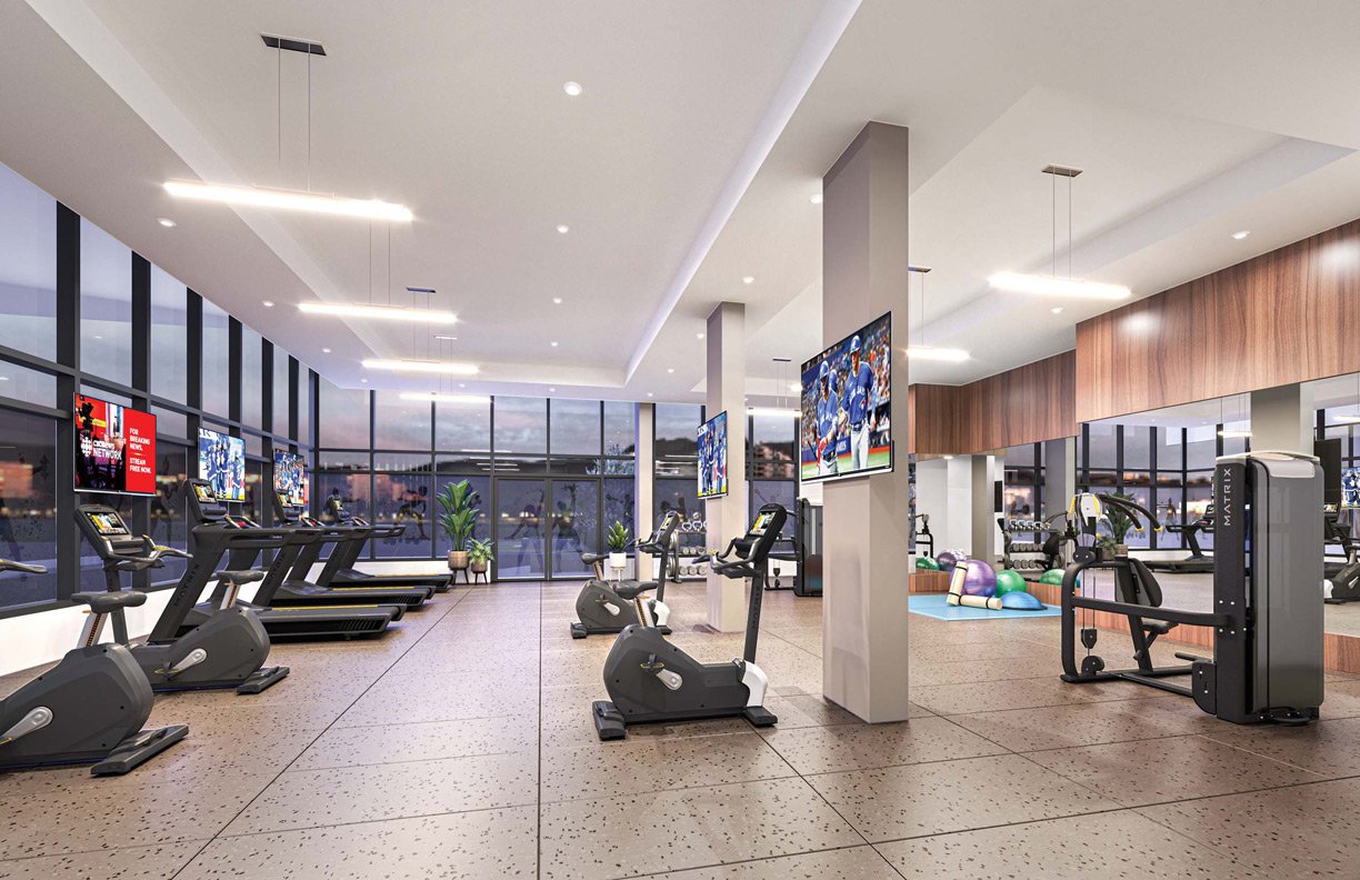 Interior of a modern gym featuring treadmills, exercise bikes, weight machines, and fitness balls. TVs mounted on walls and large windows in a well-lit space.