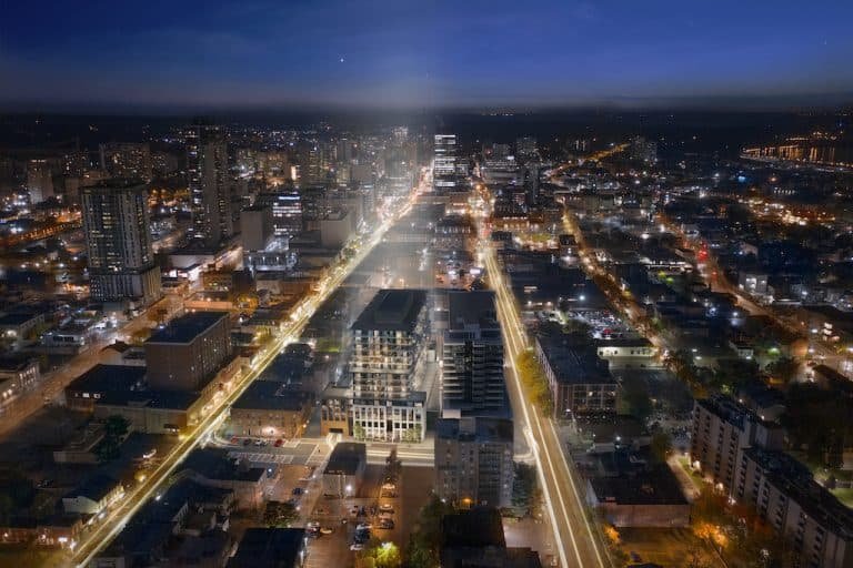 A nighttime aerial view of a city with brightly lit streets and buildings. The long exposure captures light trails of vehicles, highlighting busy roads, while the city extends outward with a mix of high-rise and low-rise structures illuminated against the dark sky. New homes in GTA are scattered among these lights.