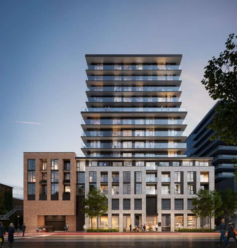 A modern mixed-use building features a sleek, reflective glass facade with multiple balconies on its upper floors. The lower floors have brick and stone exteriors. Trees line the sidewalk, and people are walking nearby at dusk, exploring the new condos in GTA available in this vibrant community.