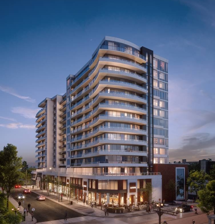 A modern, multi-story apartment building with numerous glass balconies is illuminated at dusk. The building has a sleek design with curved edges and ground-floor businesses. Surrounding it are well-lit streets, cars, trees, and pedestrians, showcasing the allure of new condos in GTA.