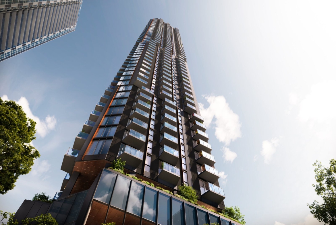 A modern skyscraper with a unique, layered architectural design, featuring a mix of reflective glass and rustic panels, rises under a clear sky, surrounded by lush greenery and new condos.