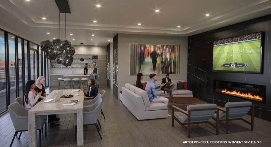A modern living space in new homes showcases a group of people seated on sofas, watching a soccer game on a large wall-mounted TV. Nearby, others gather around a dining table with laptops and papers. The room, found in pre-construction homes, boasts floor-to-ceiling windows, contemporary lighting, and a fireplace.