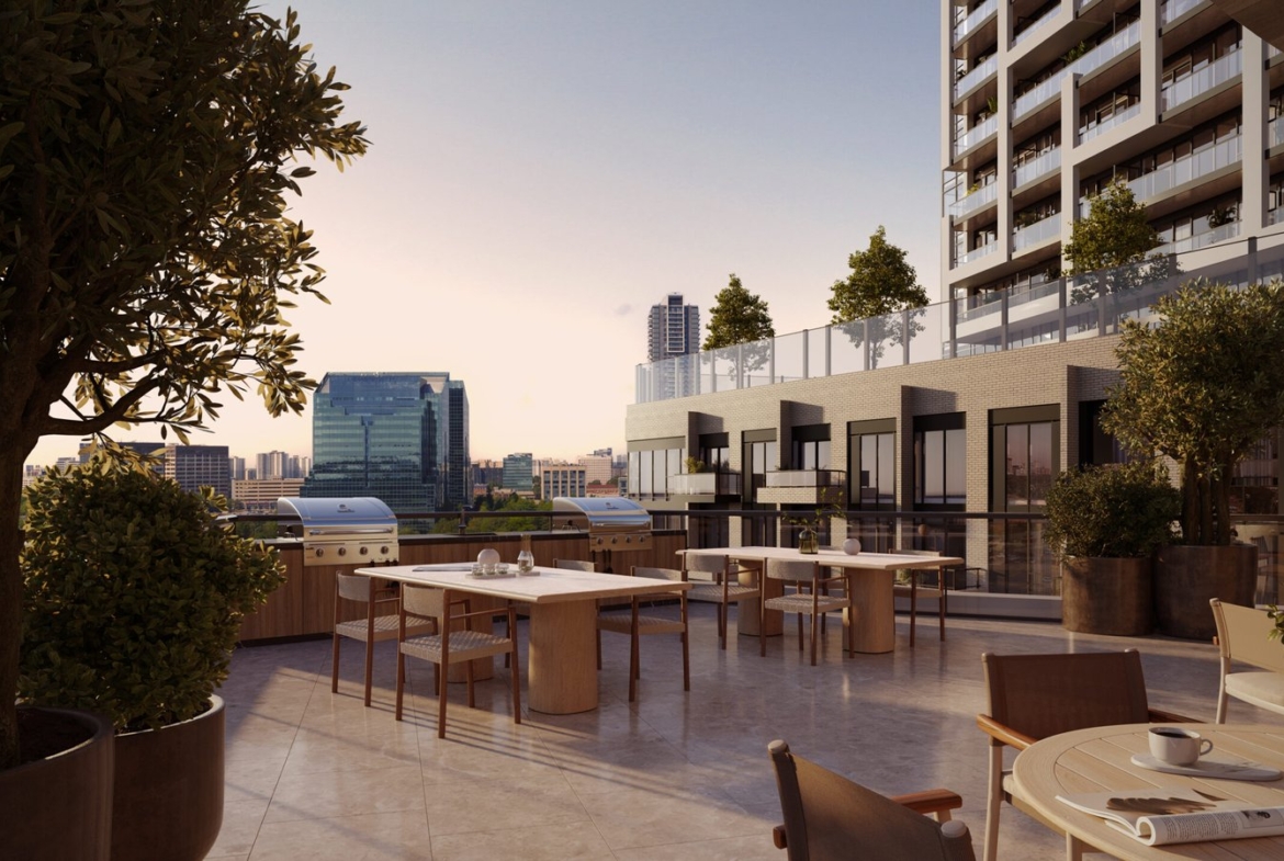 An outdoor rooftop dining area of a modern building, featuring several tables set for dining, potted plants, and overlooking a cityscape during sunset. Browse our Gagan Bector for similar views in