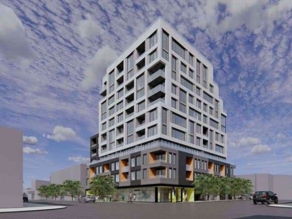 Motto Condos is a modern multi-story building with a unique geometric design, featuring protruding balconies and large windows. It stands on a street corner with a clear sky and scattered clouds above, surrounded by a few trees and vehicles nearby.