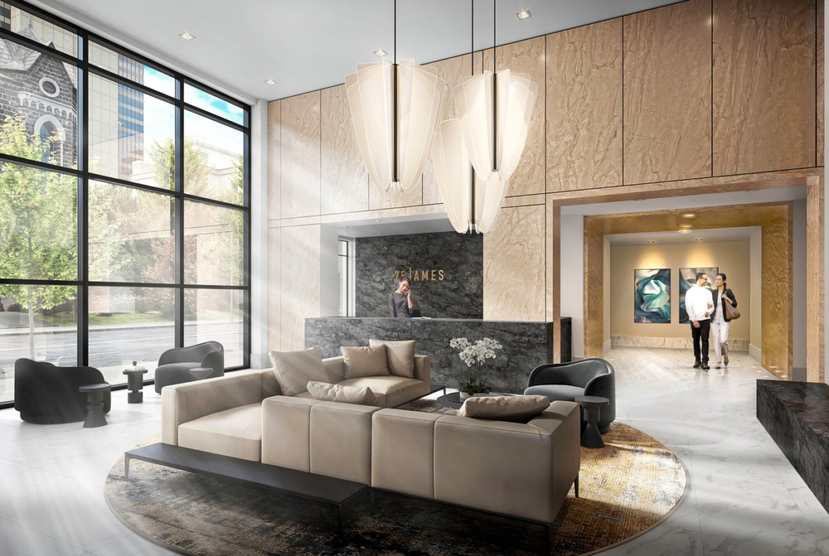 A modern, spacious lobby with large windows allowing natural light to flood in. The area, reflective of the stylish interiors found in new condos in GTA, includes beige sofas arranged around a coffee table, elegant lighting fixtures, and a chic reception desk in the background. Two people walk toward an elevator area.