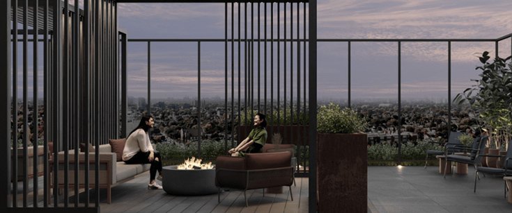 Two people sit around a fire pit on a rooftop terrace at dusk. They are surrounded by modern outdoor furniture, potted plants, and a view of new homes in the GTA sprawled out in the distance. The sky is cloudy with hues of pink and purple.