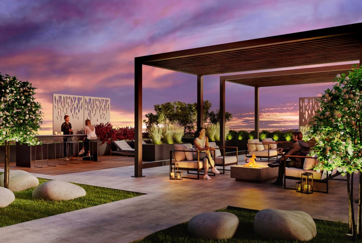 A stylish rooftop lounge at sunset features modern pergolas, comfortable seating, a fire pit, and lush greenery. People are socializing at a bar counter and sitting on armchairs, enjoying the elegantly landscaped space with ornamental rocks and illuminated panels—perfect for those considering new condos in GTA.