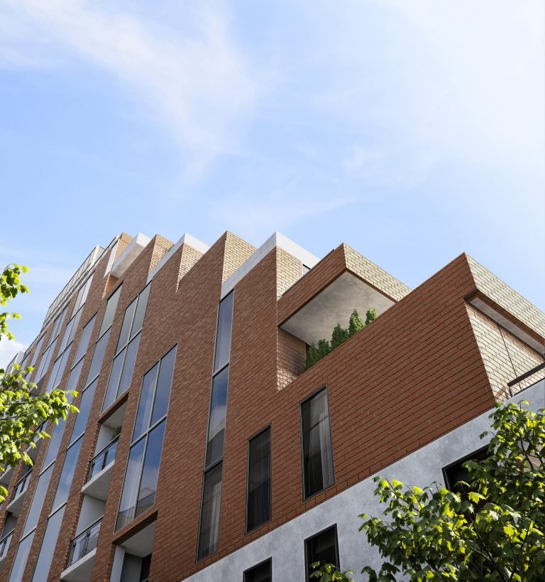 The Six99 Condos is a modern multi-story brick apartment building with large windows under a clear blue sky. The structure features sharp, angular designs with a corner balcony adorned with greenery. Trees partly frame the view, adding a natural element to the urban scene.