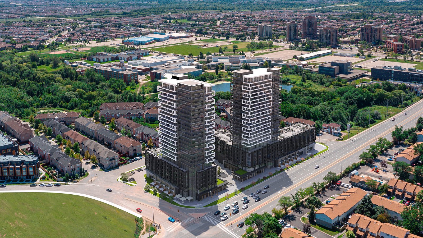 Aerial view of two tall residential towers under New condos construction beside a busy highway, surrounded by a suburban landscape with houses, smaller buildings, and patches of greenery.