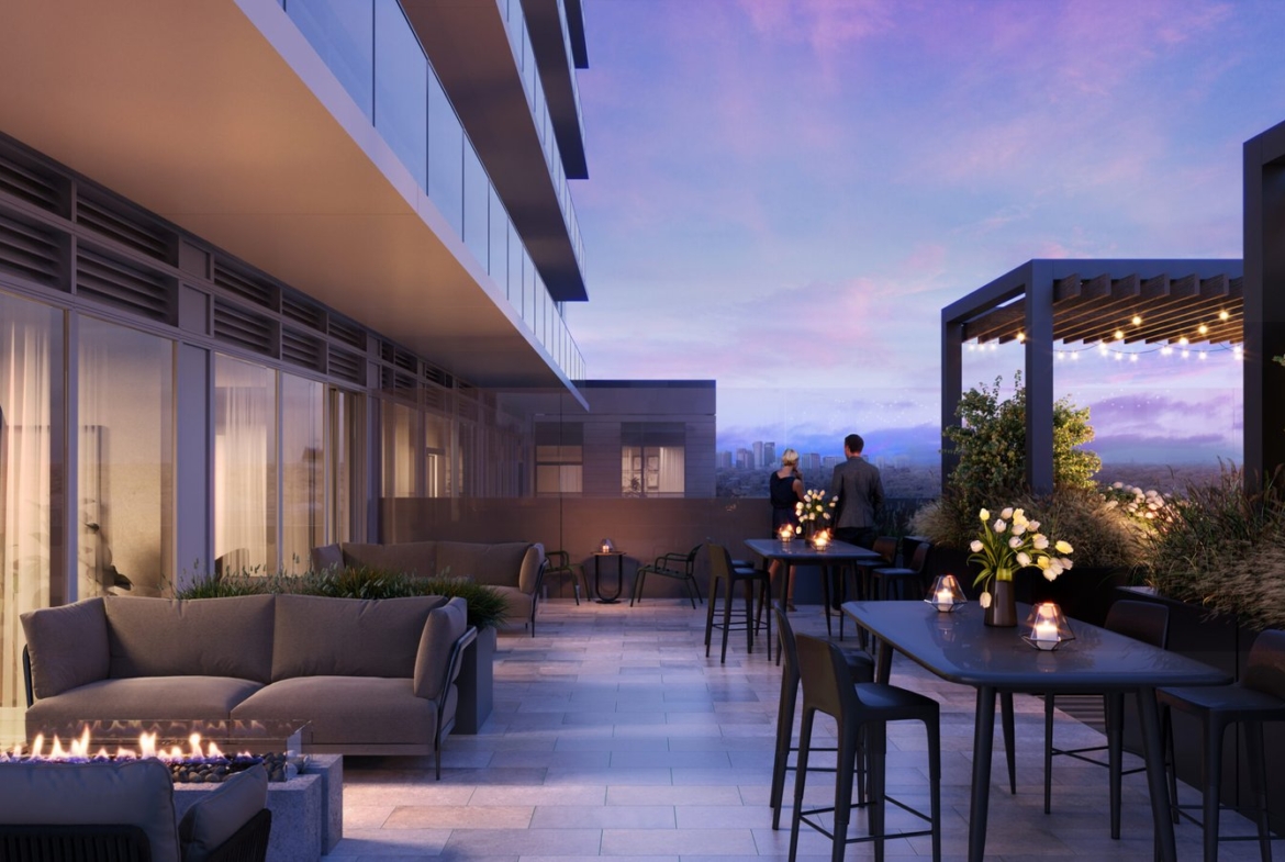 A modern outdoor rooftop terrace at dusk with stylish furniture, a fire pit, and illuminated tables. Two people admire the distant cityscape under a twilight sky, near new homes in GTA.