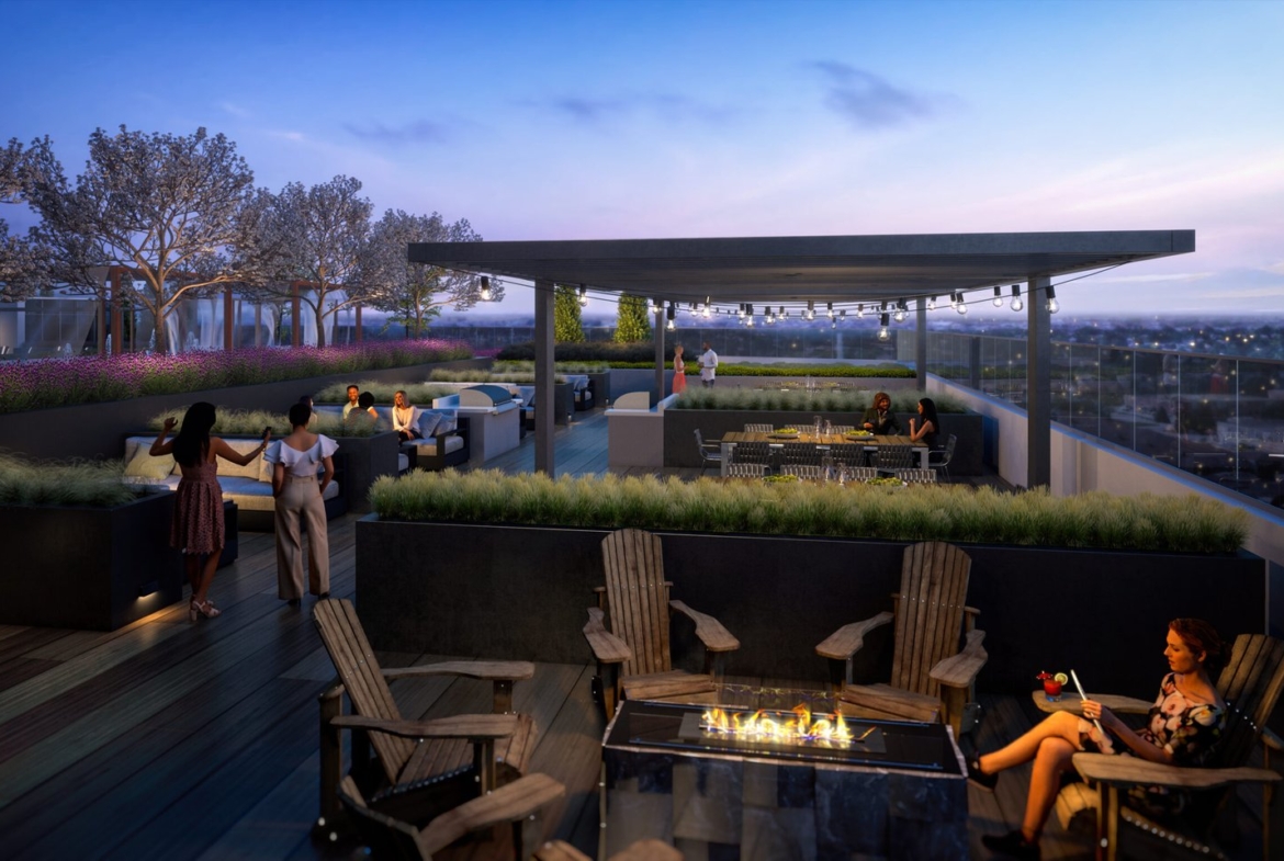 A rooftop terrace at dusk, featuring people socializing around a fire pit, sitting at tables, and enjoying the view of new condos in GTA. The space has modern furniture, plants, and string lights under a pergola, creating a cozy ambiance. Trees and a cityscape are visible in the background.