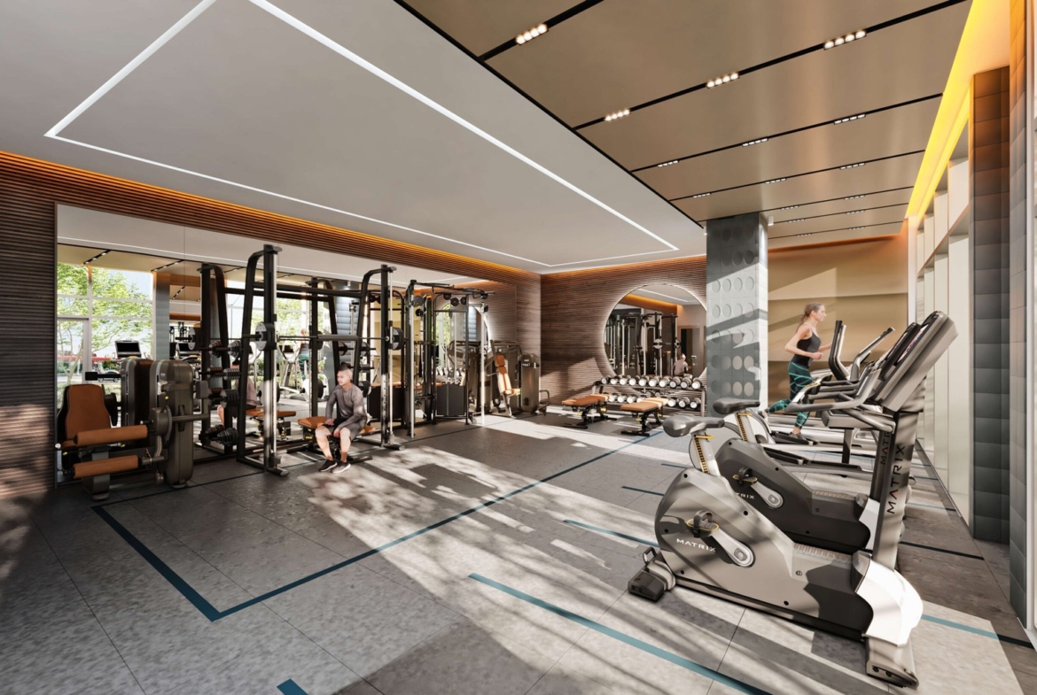 A modern gym with exercise machines, including treadmills, weightlifting equipment, and stationary bikes. A person uses the equipment as natural light streams in from large windows, creating a bright and inviting atmosphere—perfect for those living in new condos in Brampton nearby.