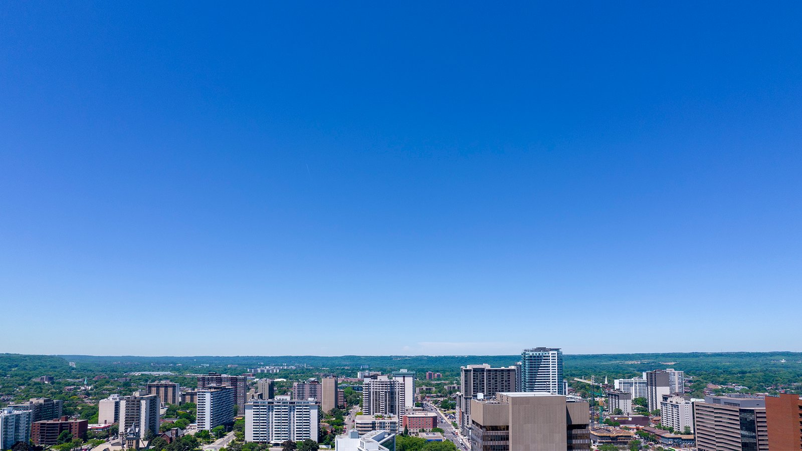 A cityscape featuring numerous high-rise buildings and skyscrapers, set against a clear blue sky. The horizon reveals green, hilly terrain in the background, blending urban and natural landscapes with new condos in GTA offering fresh perspectives on modern living. A cityscape featuring numerous high-rise buildings and skyscrapers, set against a clear blue sky. The horizon reveals green, hilly terrain in the background, blending urban and natural landscapes with new condos in GTA offering fresh perspectives on modern living.