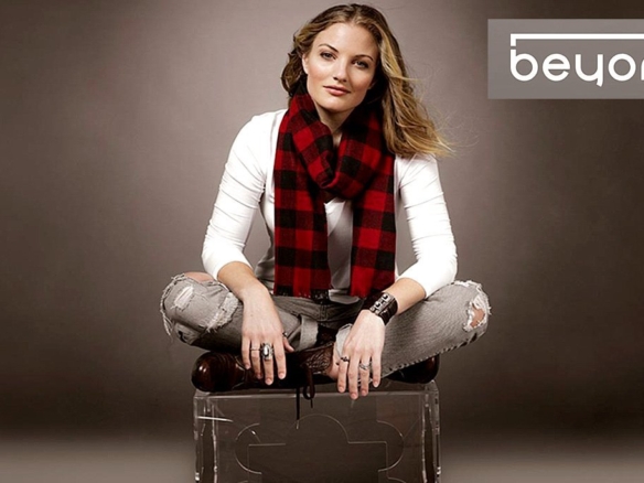 A person with long hair sits cross-legged on a transparent chair, wearing a white shirt, ripped jeans, and a red and black checkered scarf. They have a confident expression. The words "Beyond Condos" appear in the upper right corner of the image.