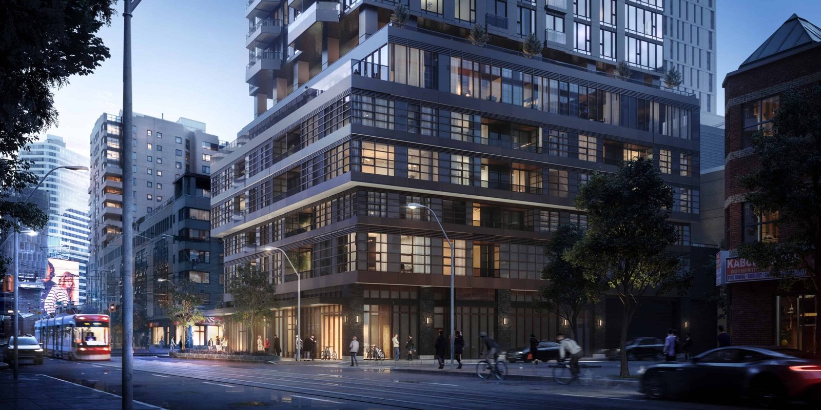 A street view captures a modern city corner at dusk, highlighting a multi-story building with glass windows aglow. Pedestrians stroll along the sidewalk as vehicles and a streetcar navigate the road. Trees line the area, complementing the urban landscape that boasts new condos in GTA.