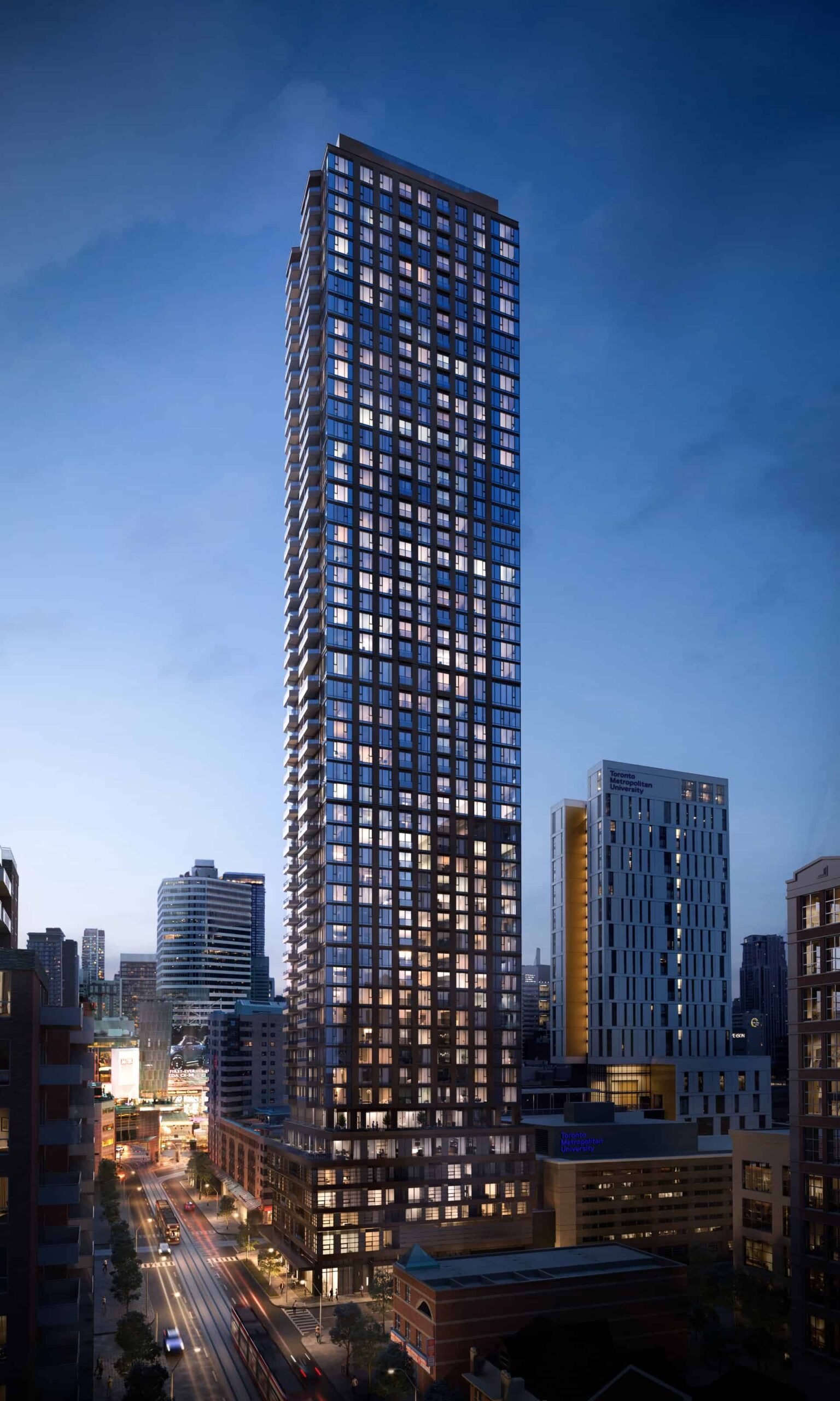 A towering skyscraper with illuminated windows stands against a twilight sky, surrounded by other buildings in a bustling urban area. Streetlights and car trails light up the busy road below, as nearby new condos in the GTA promise luxurious living above the vibrant city scene.