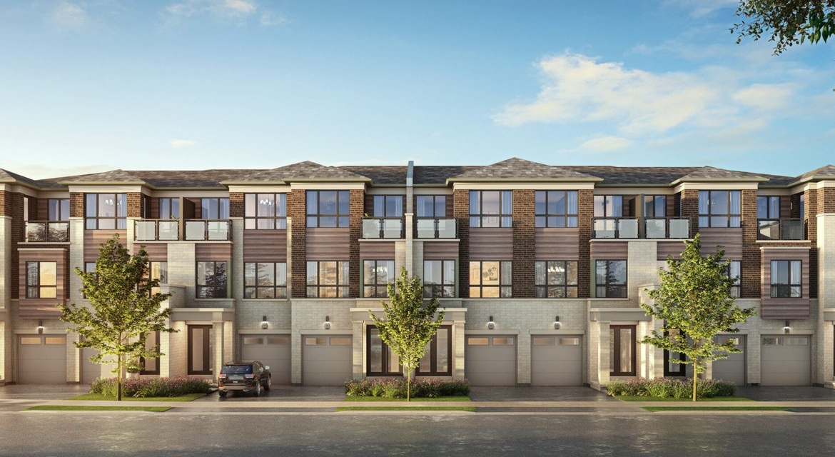 A modern three-story townhouse complex with a brick and siding exterior showcases large windows and balconies. Trees gracefully line the street, while a parked car rests in front. The sky is clear and blue, complementing these new homes in Brampton's serene setting.