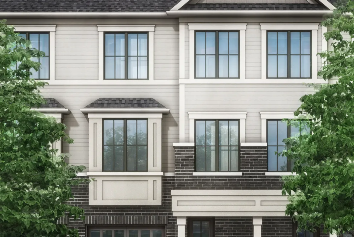 Image of a modern three-story townhouse with a gray and beige facade, large windows, and two garages. Flanked by vibrant green trees under a clear sky with scattered clouds, this residence epitomizes the charm of new homes in Brampton.