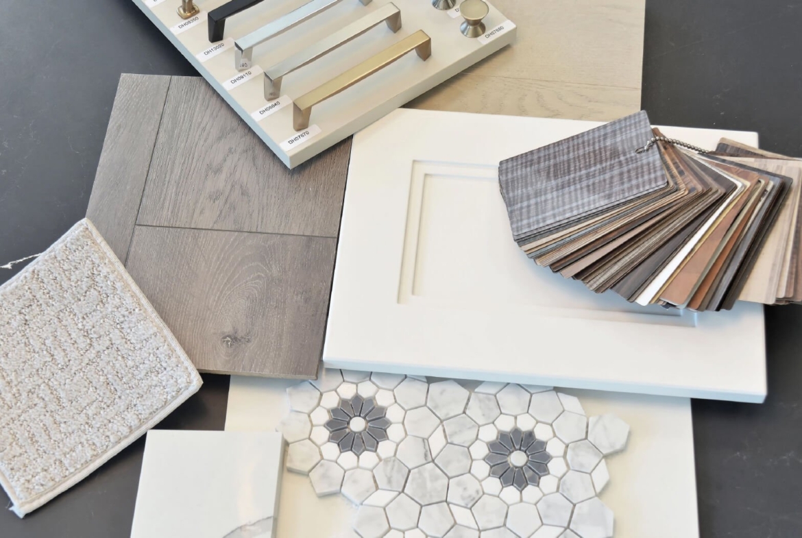 Explore a collection of interior design samples for new homes in Brampton, featuring metallic cabinet handles, wooden flooring, hexagonal marble tiles, and a textured carpet swatch. Discover a variety of colored fabric swatches and a white cabinet door displayed elegantly on a dark surface.