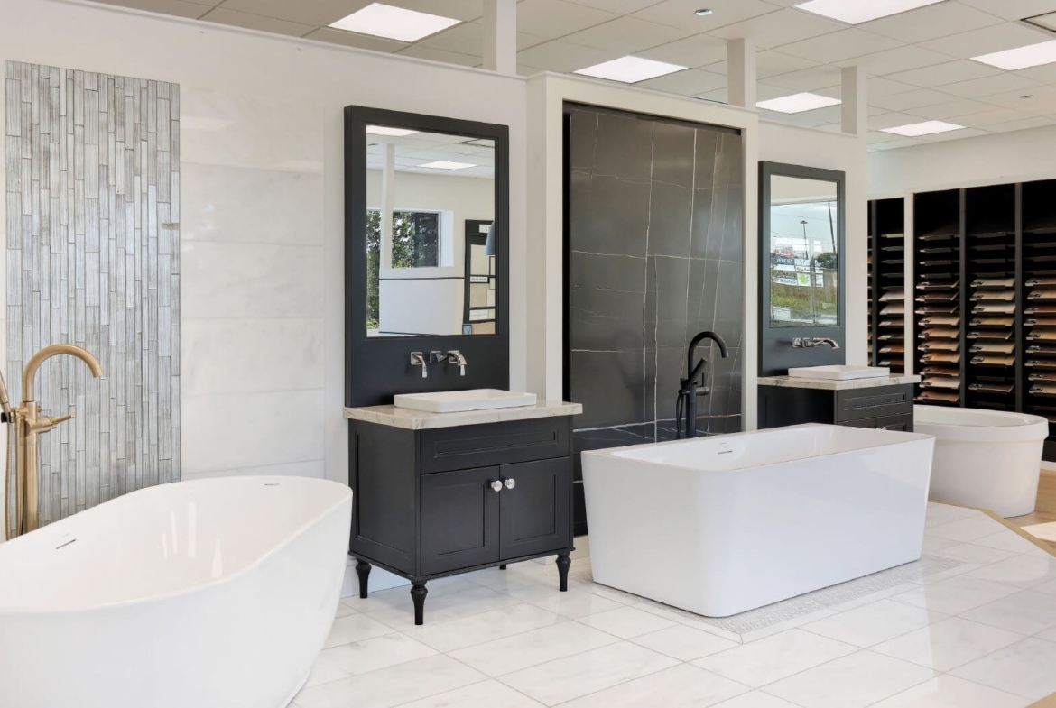A modern bathroom showroom by Royal Pine Homes in Mayfield Village features an elegant design with freestanding and rectangular tubs, black vanities paired with mirrors, chrome faucets, and a wall display of tile samples.