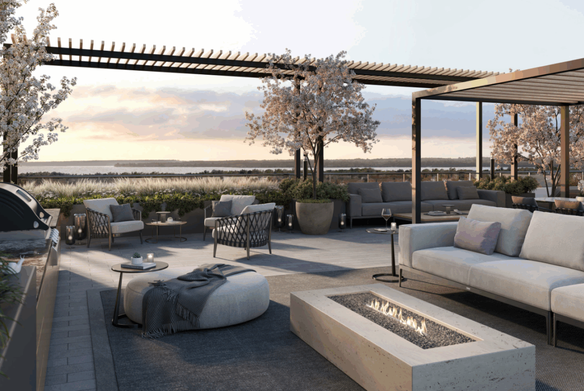 A modern rooftop patio in one of the new homes in Toronto features comfortable seating around a rectangular fire pit. Blossoming trees and potted plants decorate the space. The setting sun casts a warm glow over the relaxed ambiance, with a view of nature in the background.