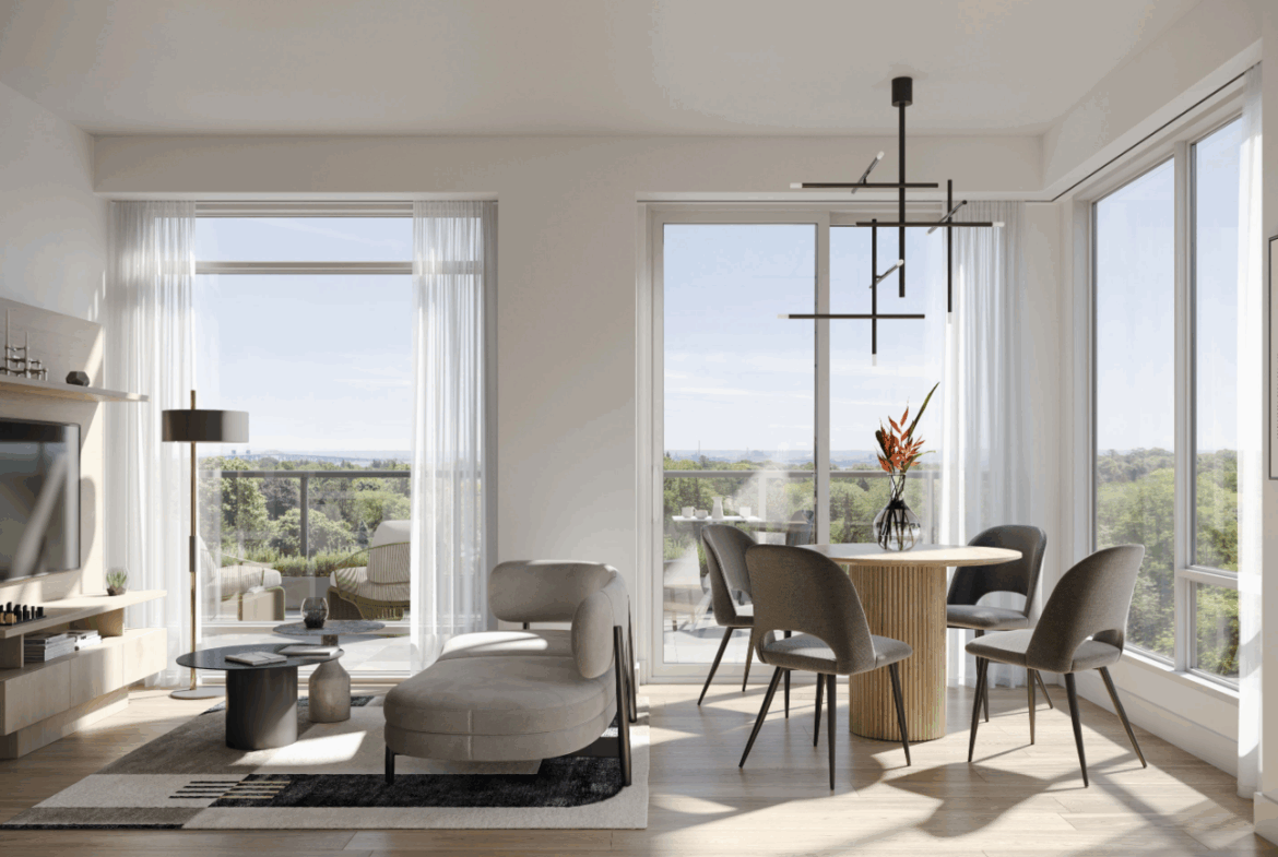 A modern living room with large windows overlooking a scenic view. The room features a cozy sofa, a small coffee table, and a round dining table with chairs. A contemporary chandelier hangs from the ceiling, and a vase with flowers decorates the table—perfect for those exploring new condos in Brampton.