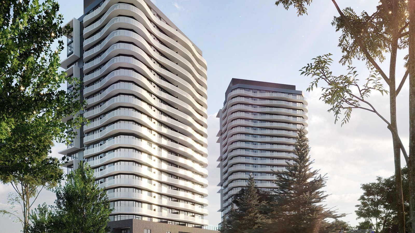 Two modern high-rise buildings with curved balconies stand under a clear sky. The structures, surrounded by trees, add a touch of greenery to this urban setting. Sunlight casts soft shadows on the facades of these new condos in Brampton, offering an impressive blend of nature and architecture.