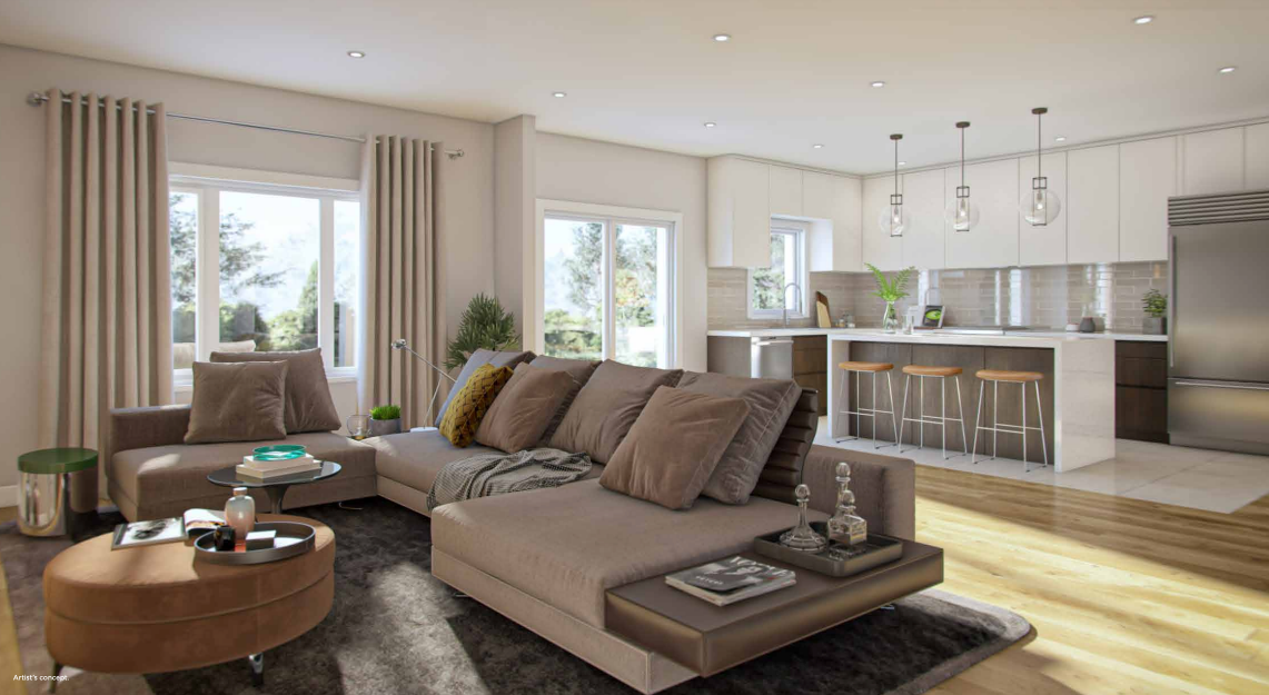 Discover a modern living room in this new home in Brampton, featuring a beige sectional sofa with brown pillows centered around a round coffee table. Large windows flood the space with natural light, and the open kitchen boasts bar stools at a counter and sleek stainless steel appliances.