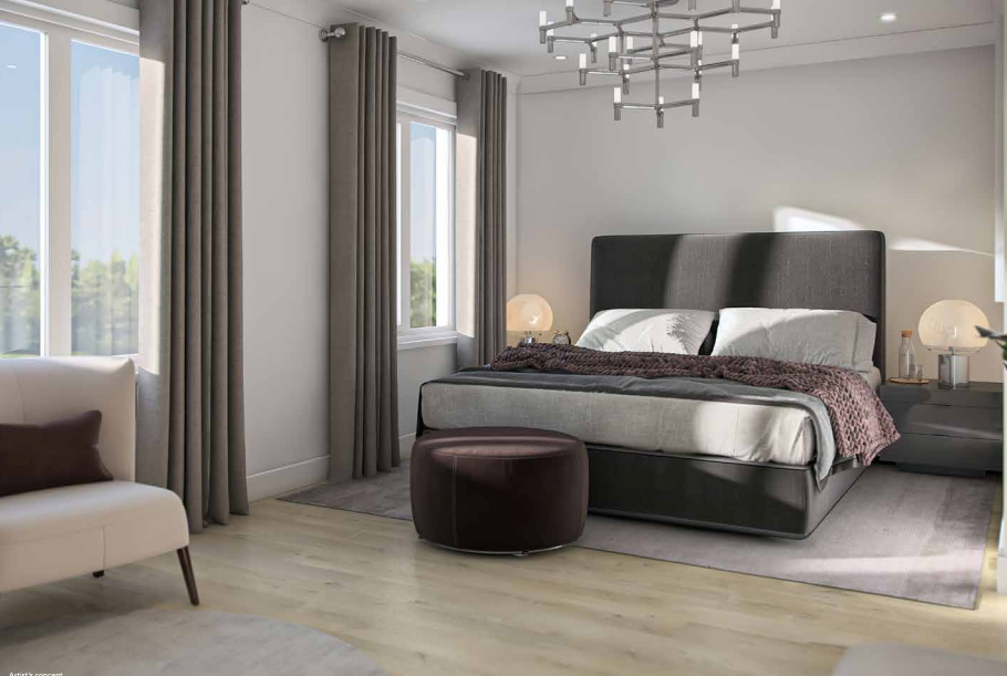 A modern bedroom in new homes features a large, dark grey upholstered bed with white and grey bedding complemented by a brown throw blanket. A stylish chandelier, round brown ottoman, cream chair, and two nightstands with lamps add elegance. Large windows with grey curtains invite natural light.