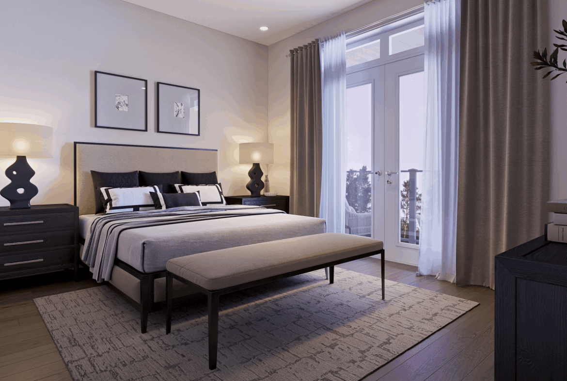 A cozy bedroom in new homes features a double bed with a gray and white striped duvet, flanked by two bedside tables with matching lamps. A bench sits at the foot of the bed, while framed art hangs above. Soft light pours through a large window with curtains, adding to the room's charm.