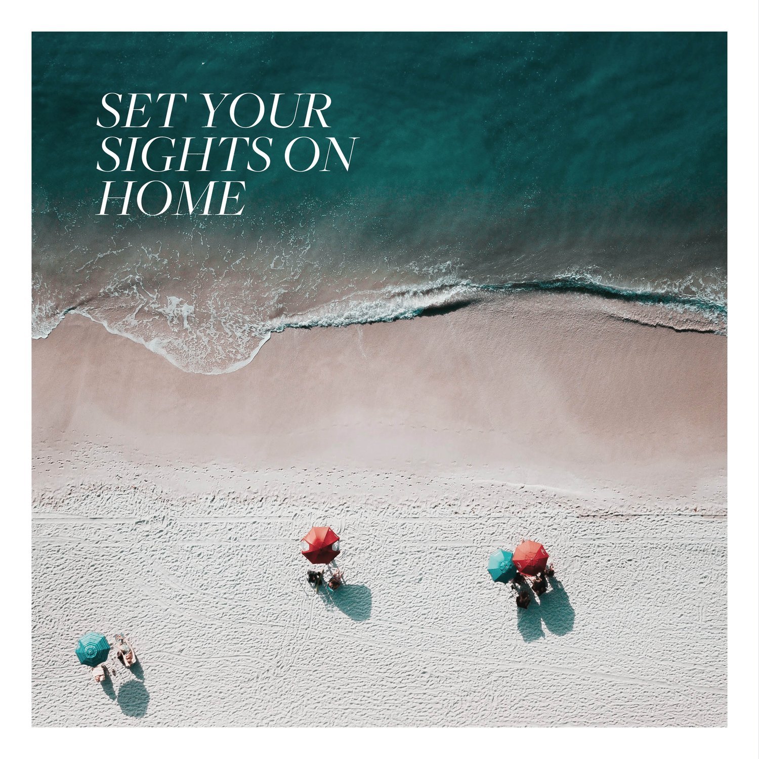 An aerial view of a sandy beach with three people under red and green umbrellas near the water's edge. Text on the image reads, "Set Your Sights on Home." Waves gently lap the shore, inviting you to dream of new homes in Toronto.