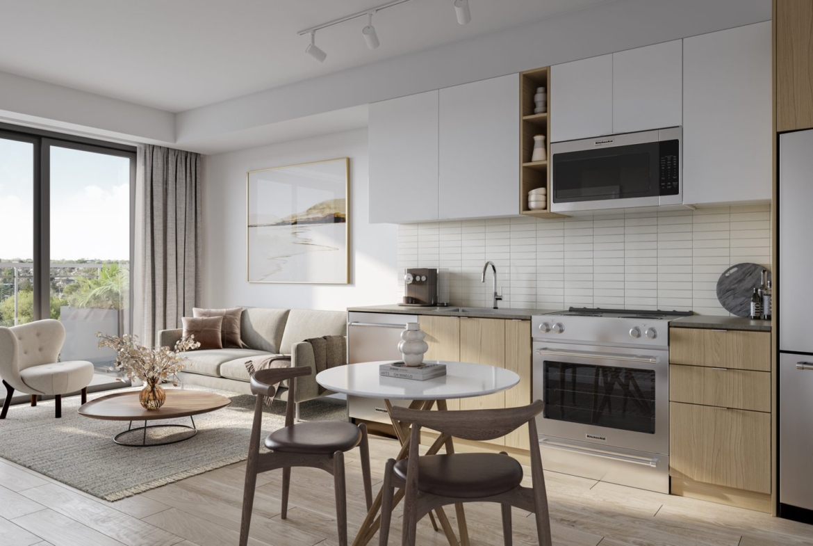 Explore the modern kitchen and living area with light wooden floors, featuring white cabinets, a stainless steel oven and microwave, and a round dining table. A large window floods the space with natural light into this cozy haven, ideal for new homes in Toronto.