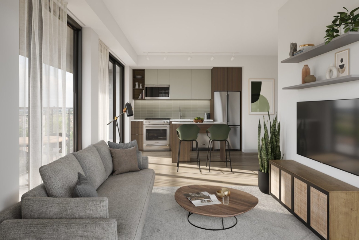 A modern living room and kitchen area with floor-to-ceiling windows in one of Toronto's new homes. It features a gray sofa, round wooden coffee table, wall-mounted TV, and a kitchen with green and brown cabinets. A plant and bar stools add accents to the space.