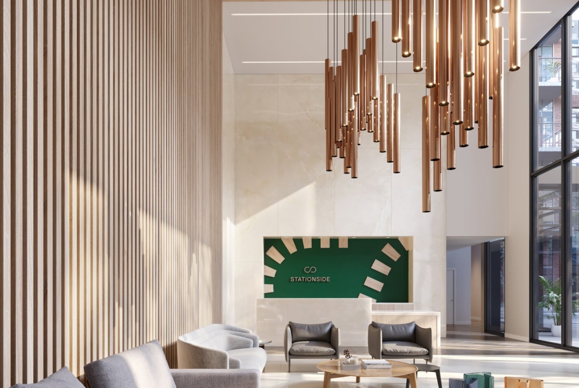 A modern lobby with wood paneling features a large hanging light fixture, gray couches, and a round wooden coffee table. A green sign with white graphics is on the far wall, and large windows flood the space with natural light—echoing the elegance of new condos in Brampton.