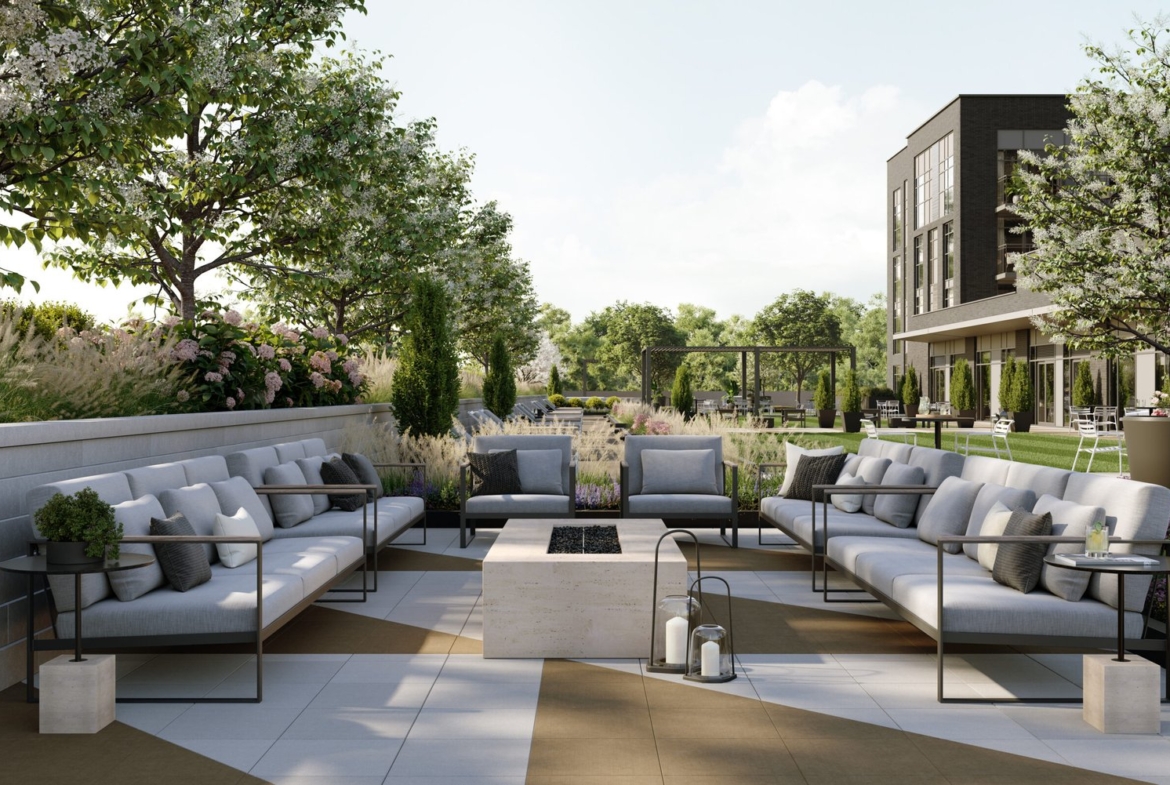 A modern outdoor patio features sleek gray sofas encircling a central rectangular stone fire pit. Adorned with potted plants and lanterns, this serene setting is enriched by the backdrop of trees and a contemporary building, ideal for new homes in Toronto.