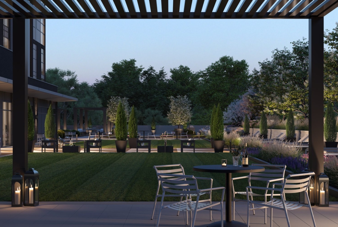 A modern outdoor patio at dusk features metal chairs and tables, embraced by lush greenery and tall potted plants. Soft lighting and lanterns add coziness. In the background, trees frame a softly lit building, hinting at the elegance of new homes.