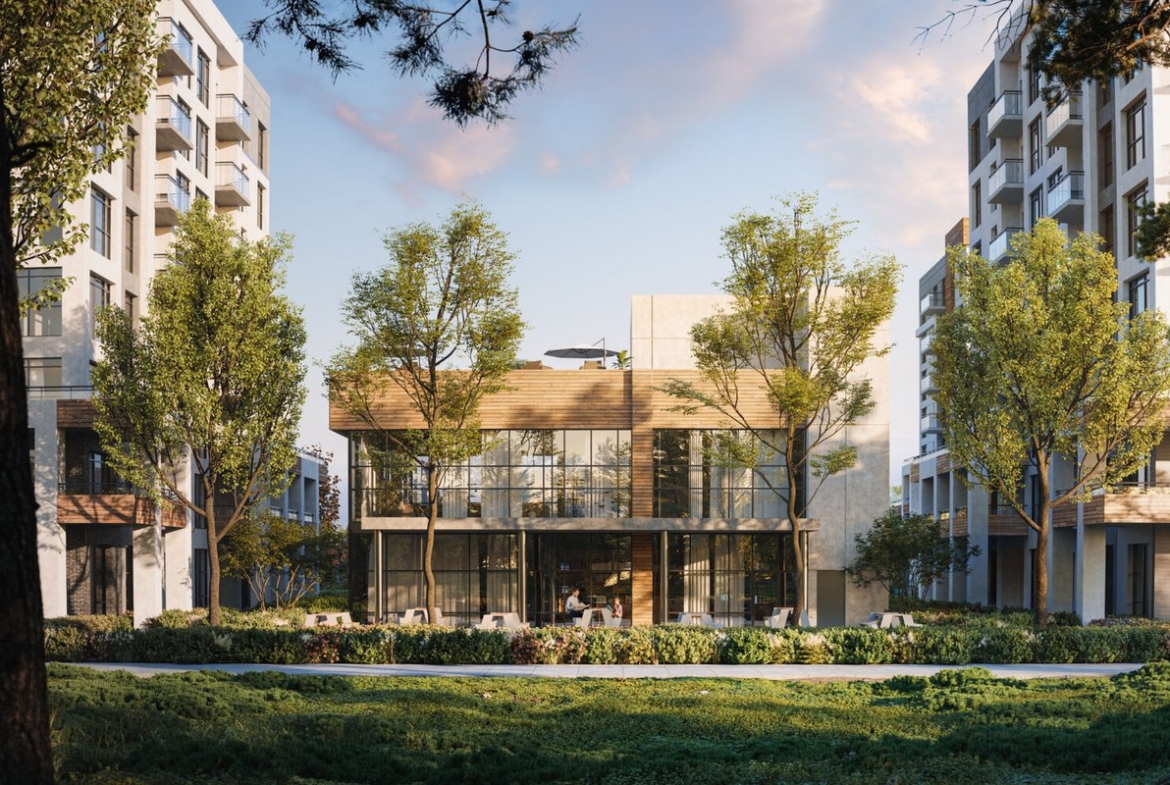 The modern, glass-fronted building, known as Mile & Creek Condos, is surrounded by lush trees and flanked by two towering residential structures. Set under a partly cloudy sky, grass and vibrant plants enhance the scenic foreground.