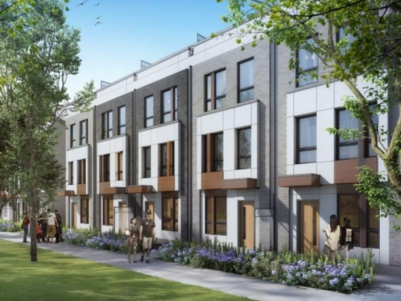 Joy Station Towns is a modern townhouse complex with three-story buildings featuring large windows and balconies. People stroll along the sidewalk bordered by trees and greenery on a sunny day.