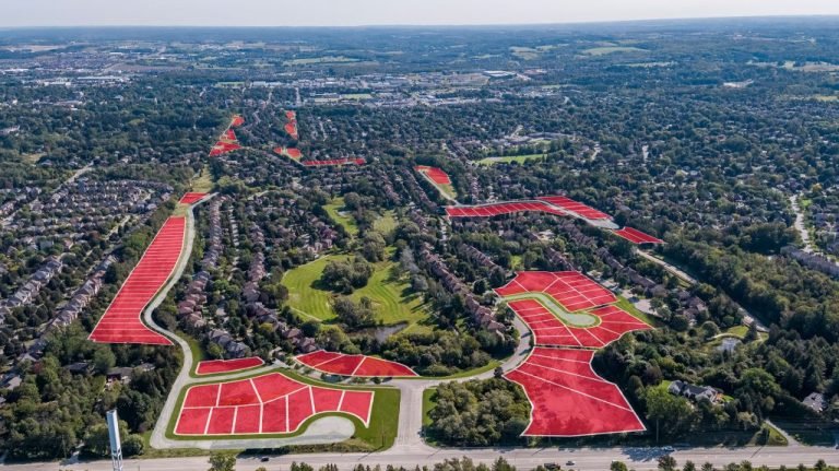 Aerial view of a suburban area with numerous houses surrounded by trees, featuring sections highlighted in red to indicate future development of pre-construction homes. Roads and lush greenery weave through this picturesque scene, promising vibrant new communities.