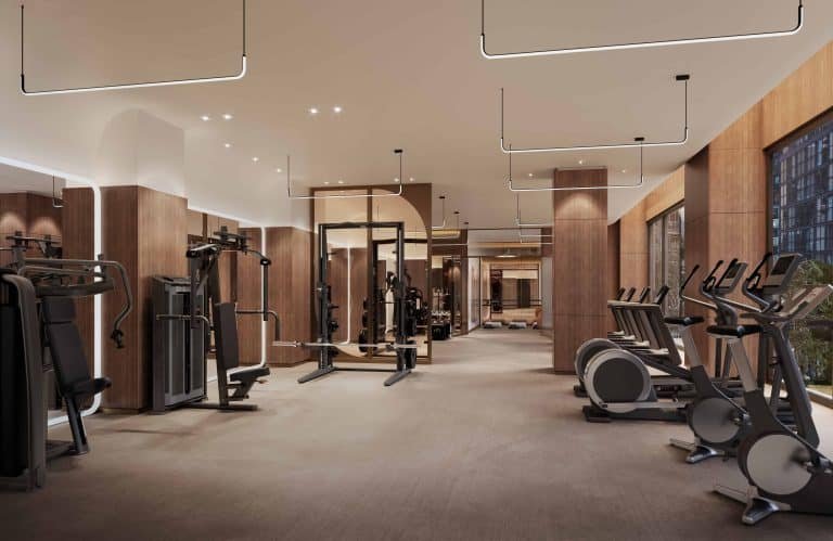 A modern gym at 101 Spadina Condos with wooden accents features various exercise equipment, including treadmills, ellipticals, weight machines, and free weights. Large windows allow natural light to illuminate the minimalist room with ceiling lights.