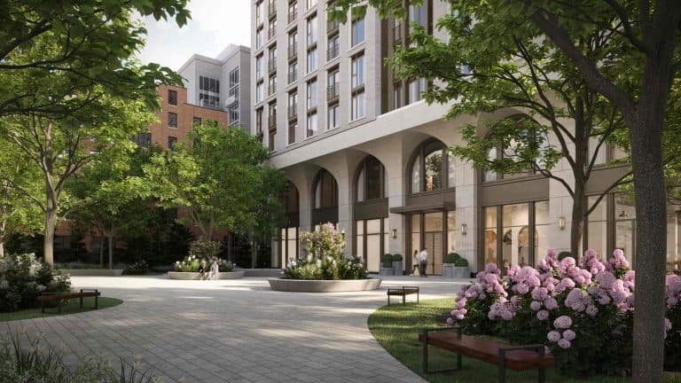 The 101 Spadina Condos boast a modern apartment building with arched entrances, surrounded by lush greenery. A paved walkway in the foreground is flanked by flower beds of pink hydrangeas and benches, while trees provide shade, creating a serene, inviting atmosphere.