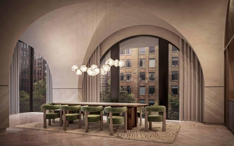 A modern dining room at 101 Spadina Condos features an arched ceiling and large windows with city views. A wooden dining table is surrounded by green upholstered chairs, and contemporary pendant lights hang above it. The room boasts a herringbone wood floor and a beige color scheme.